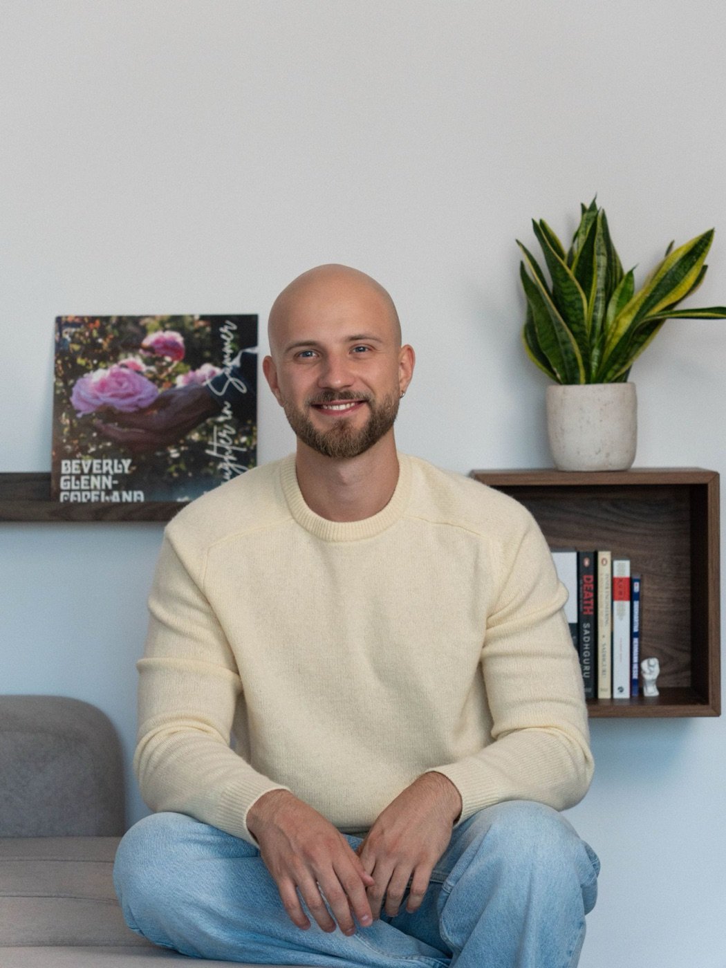 Andrii Baraniuk, smiling, sitting in front of a shelf with books and a plant